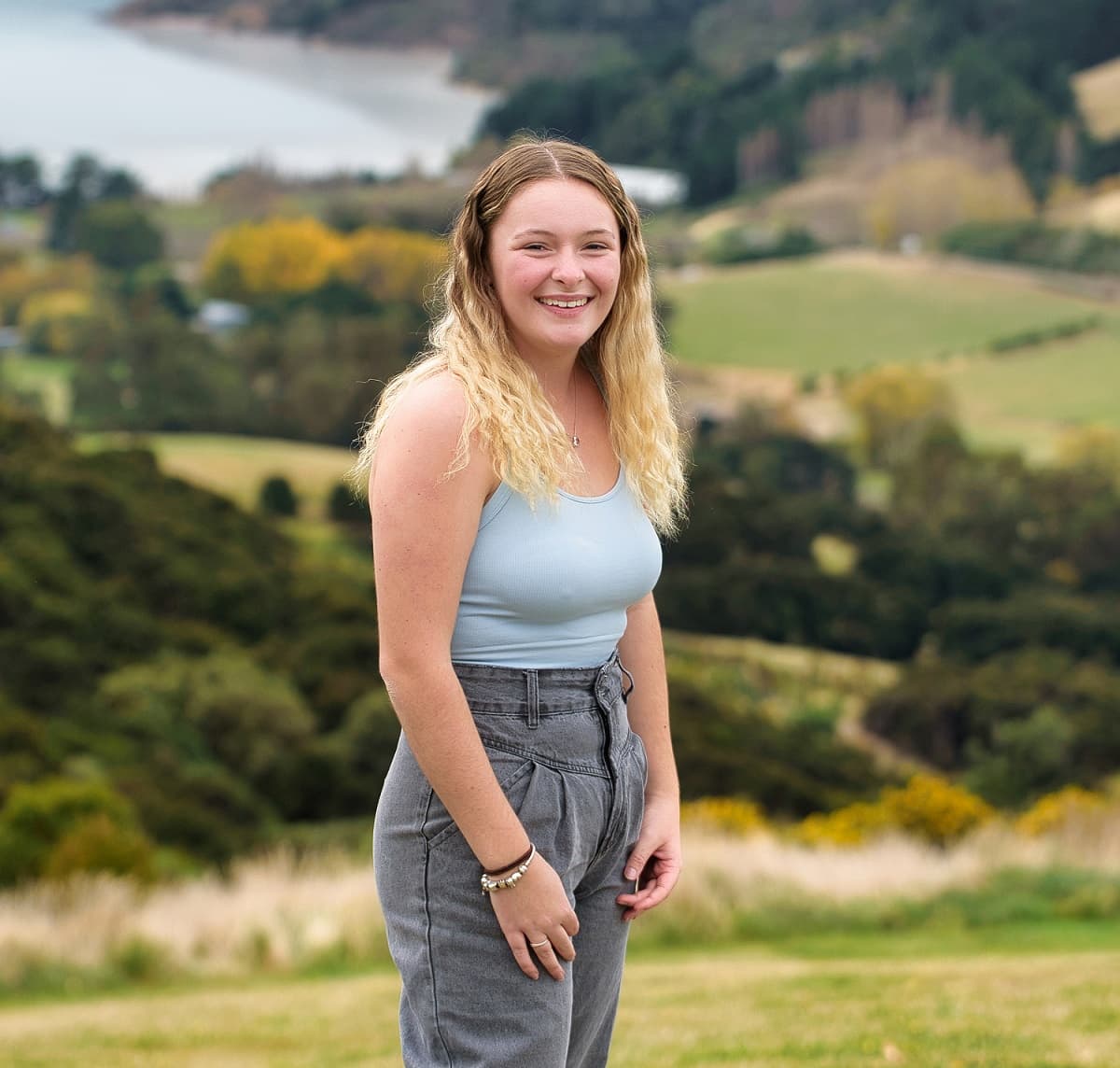 abby standing in front of a green landscape and she is smiling at the camera