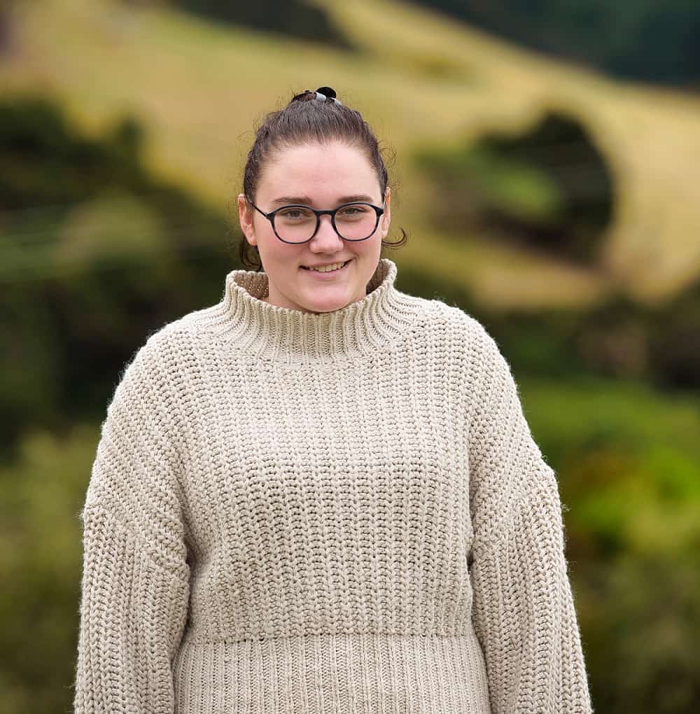bailee wearing a beige sweater and wearing glasses. she is smiling at the camera