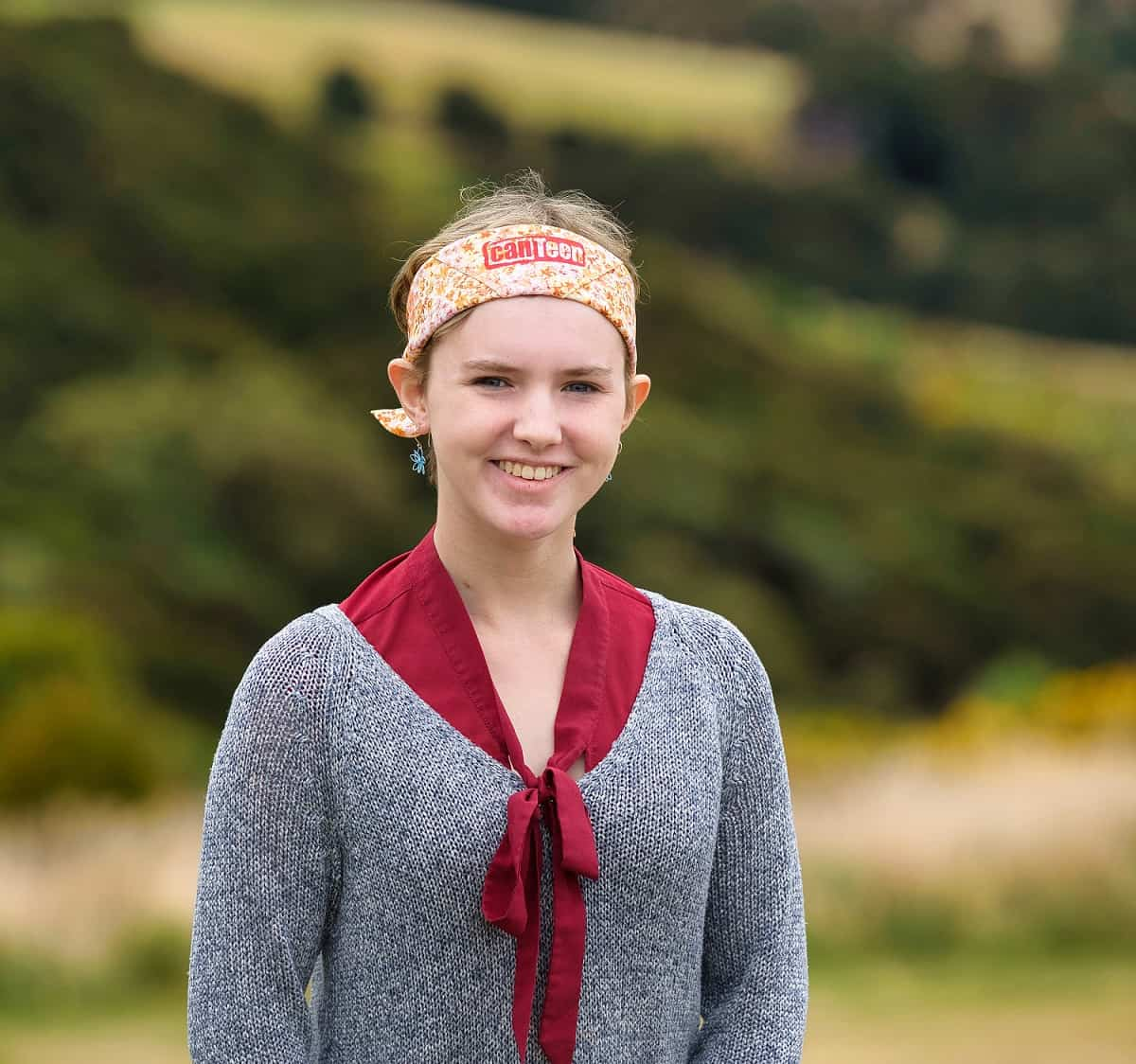 lara wearing a canteen bandanna on her head and is wearing a grey sweater. she is smiling at the camera