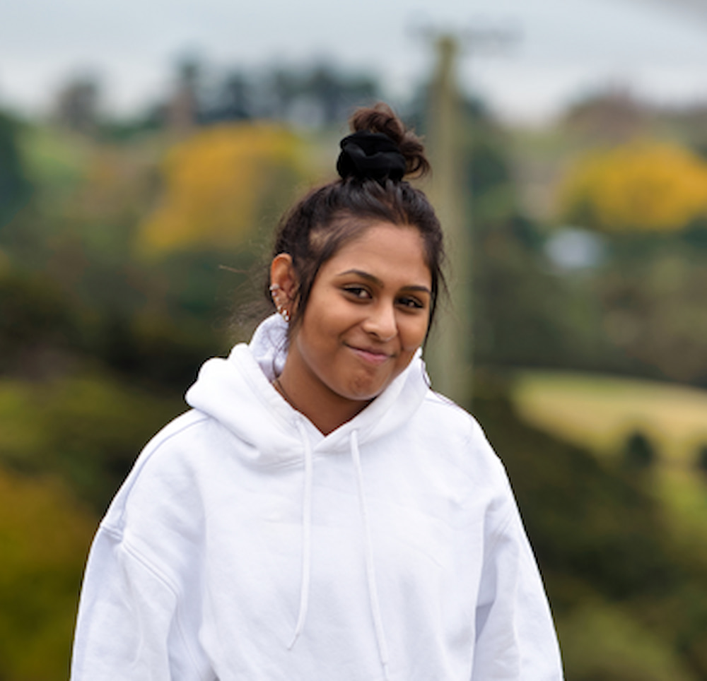 Nikhita wearing a white hoodie and has her hair in a bun. She is smiling at the camera