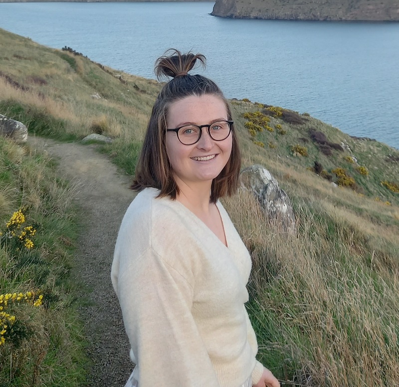 Megan smiling standing in front of hills and a lake