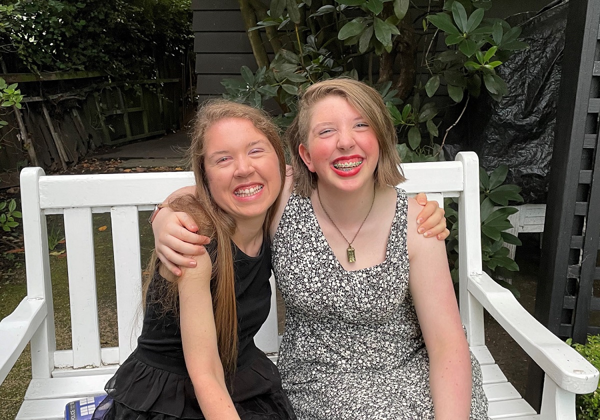 Christina and her sister sitting on a bench smiling