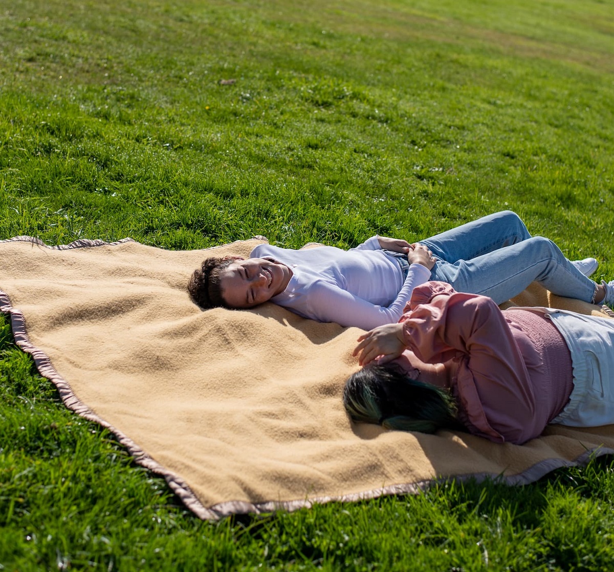 two young people impacted by cancer are laying on a picnic rug and laughing