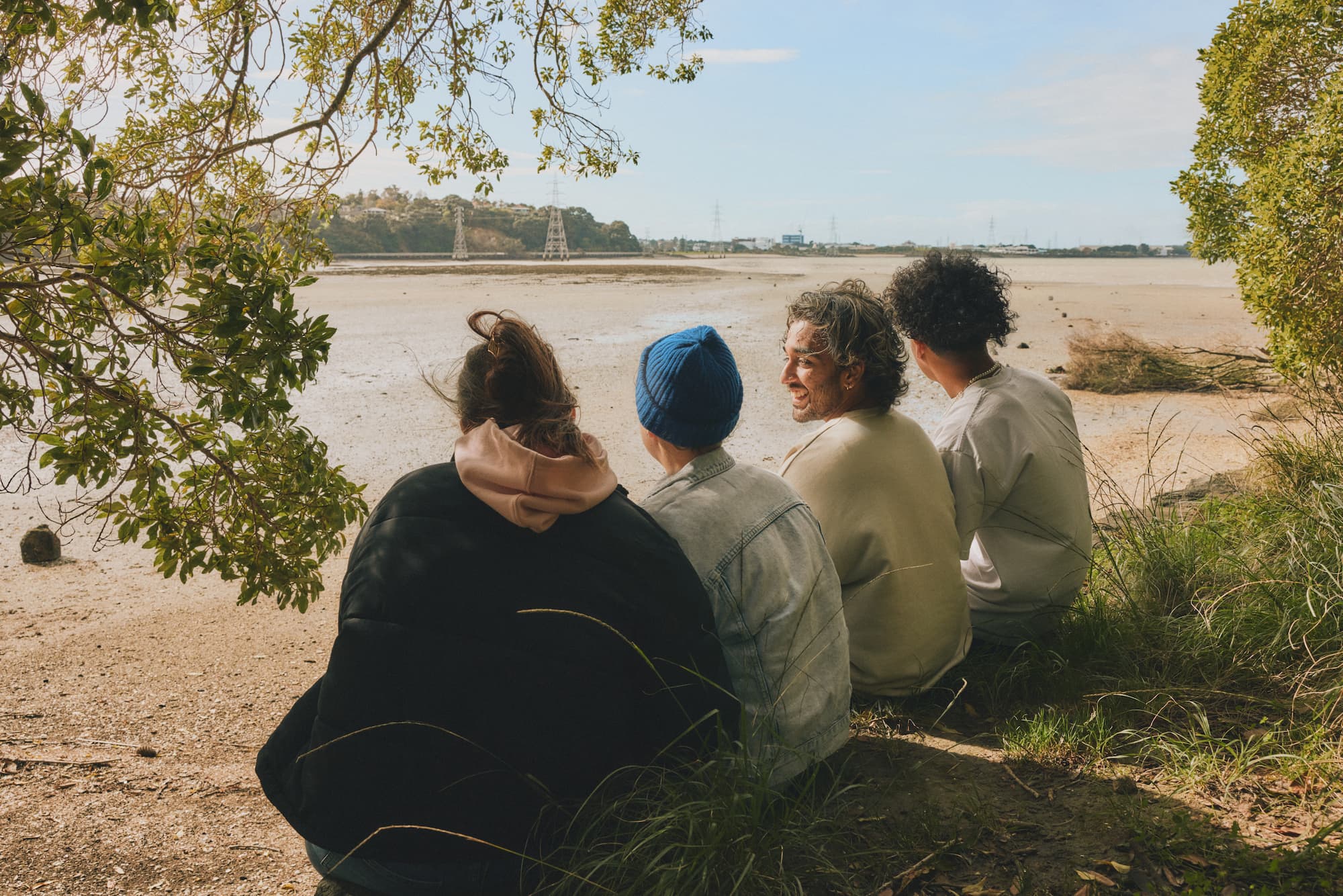 four young people sitting next to each other at the beach