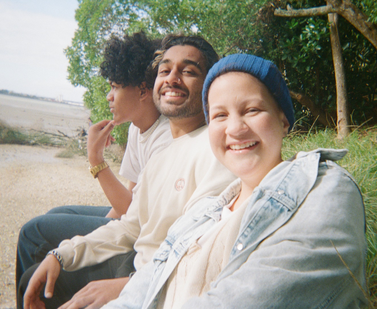 three young people impacted by cancer sitting next to each other at the beach