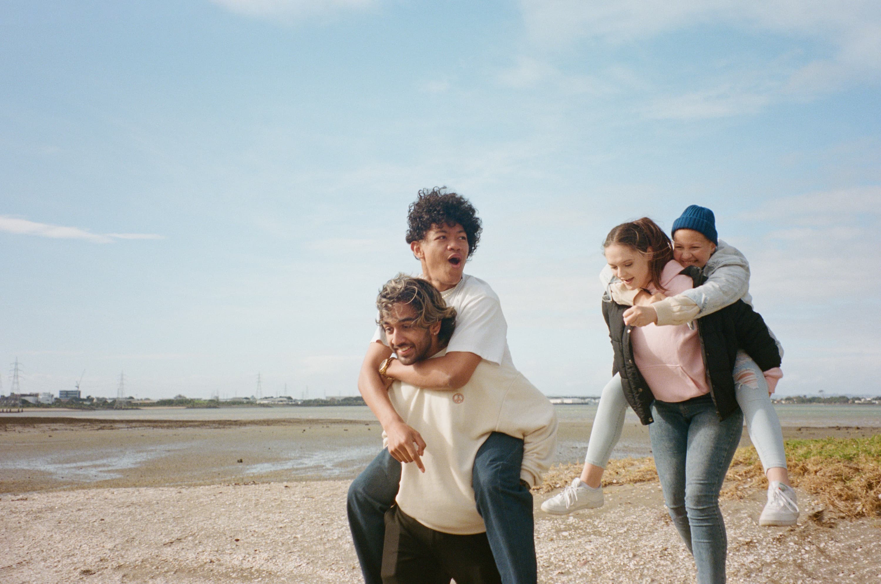 four young people giving each other piggy backs at the beach