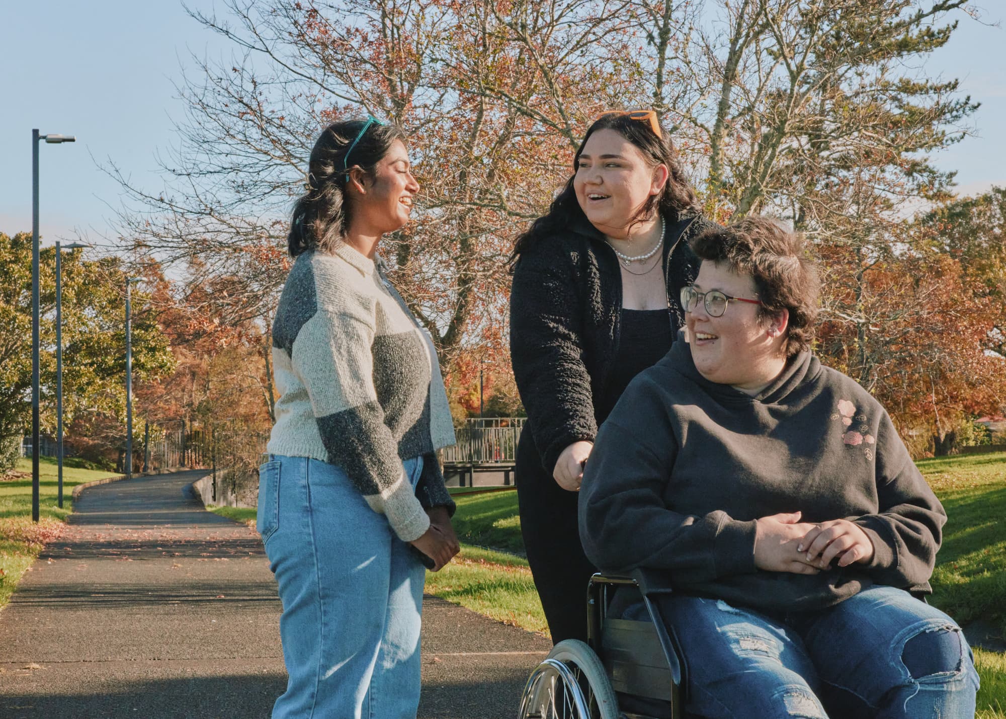 young person in a wheel chair with two friends on a walk in the park