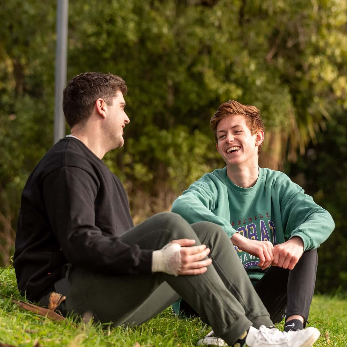 two young people sitting on the grass at a park and having a conversation