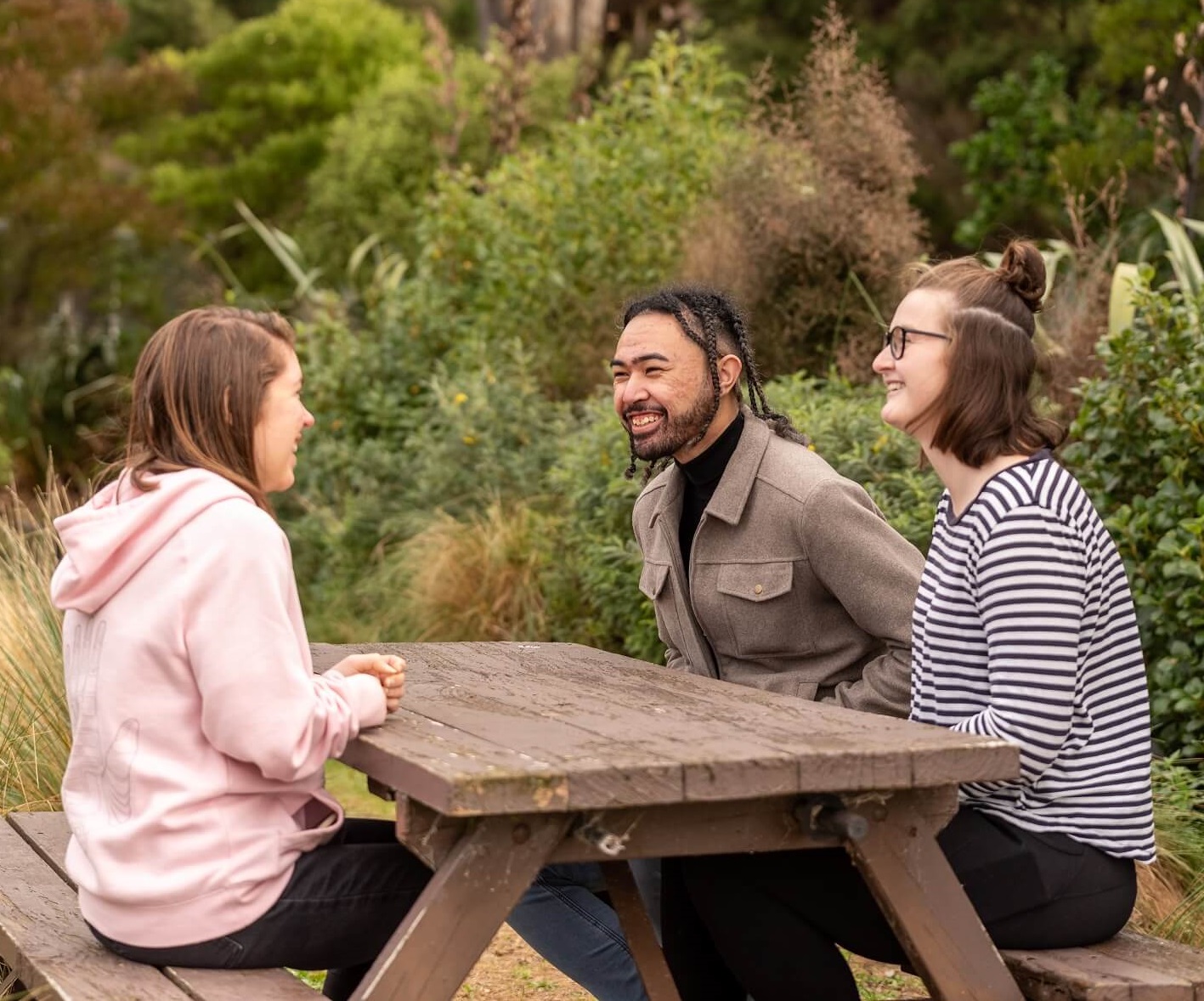 three young people sitting at a picnic table and talking