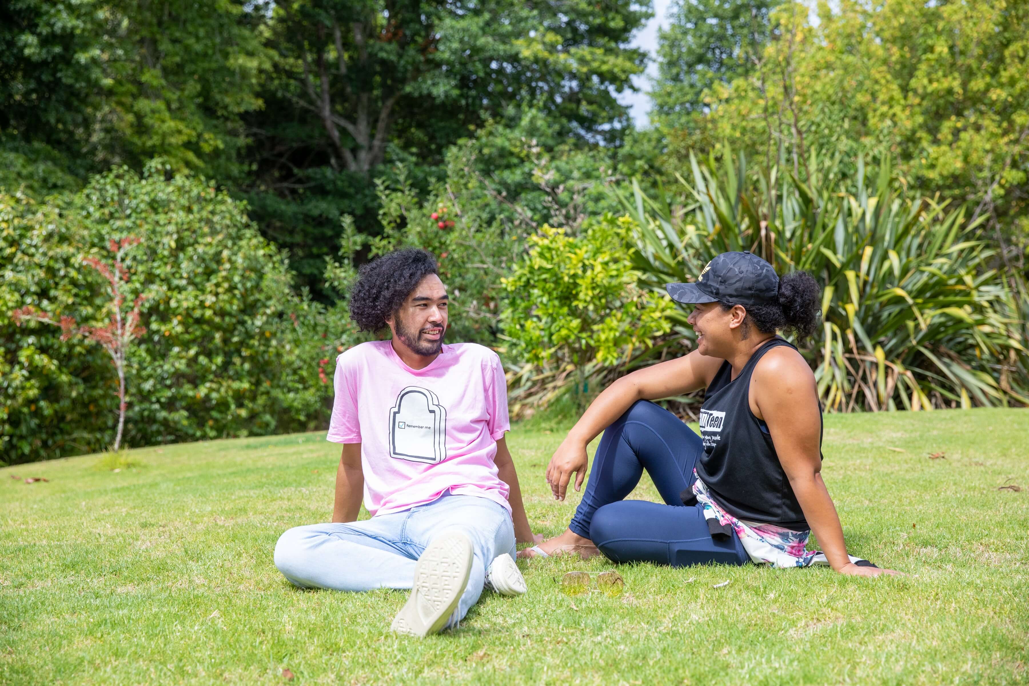 two young people sitting on the grass at a park and having a conversation
