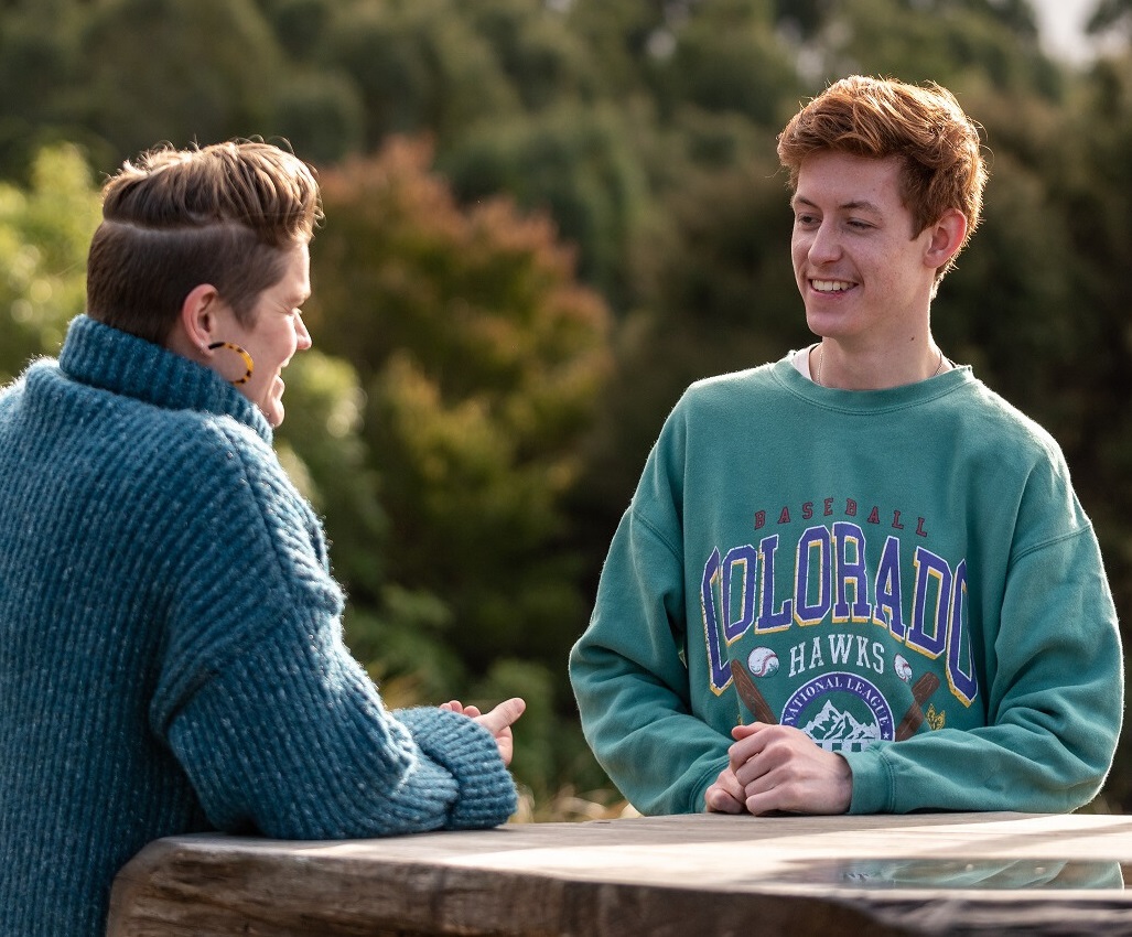 Young person impacted by teenage cancer sitting on a bench and getting cancer support by talking to someone 