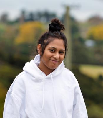 Nikhita wearing a white hoodie and has her hair in a bun. She is smiling at the camera