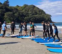 Rangatahi standing on the beach next to surfboards for a surfing lesson at CanSurf, a camp for young people impacted by cancer